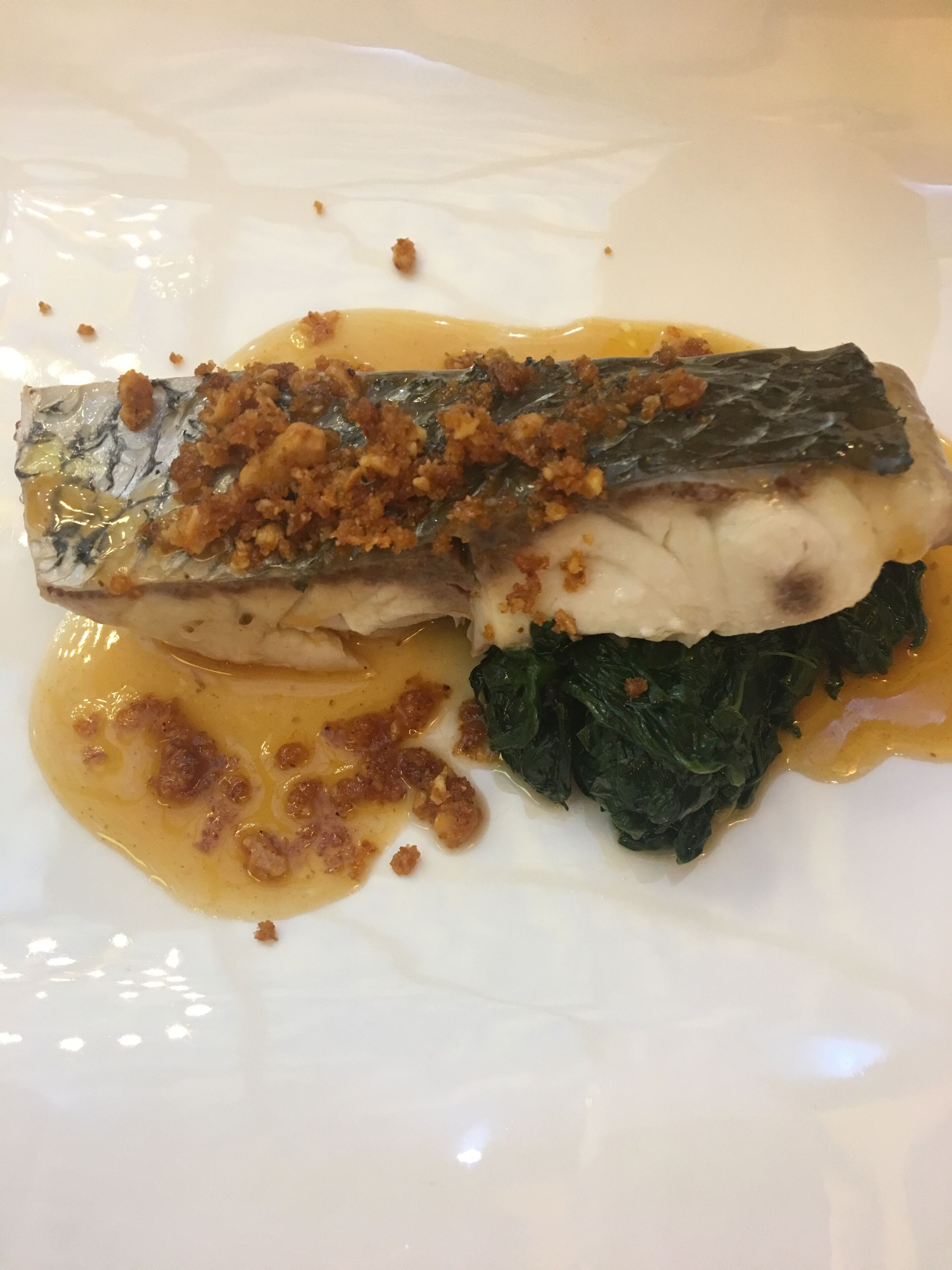 Un plato con un filete de pescado, vegetales verdes y salsa.