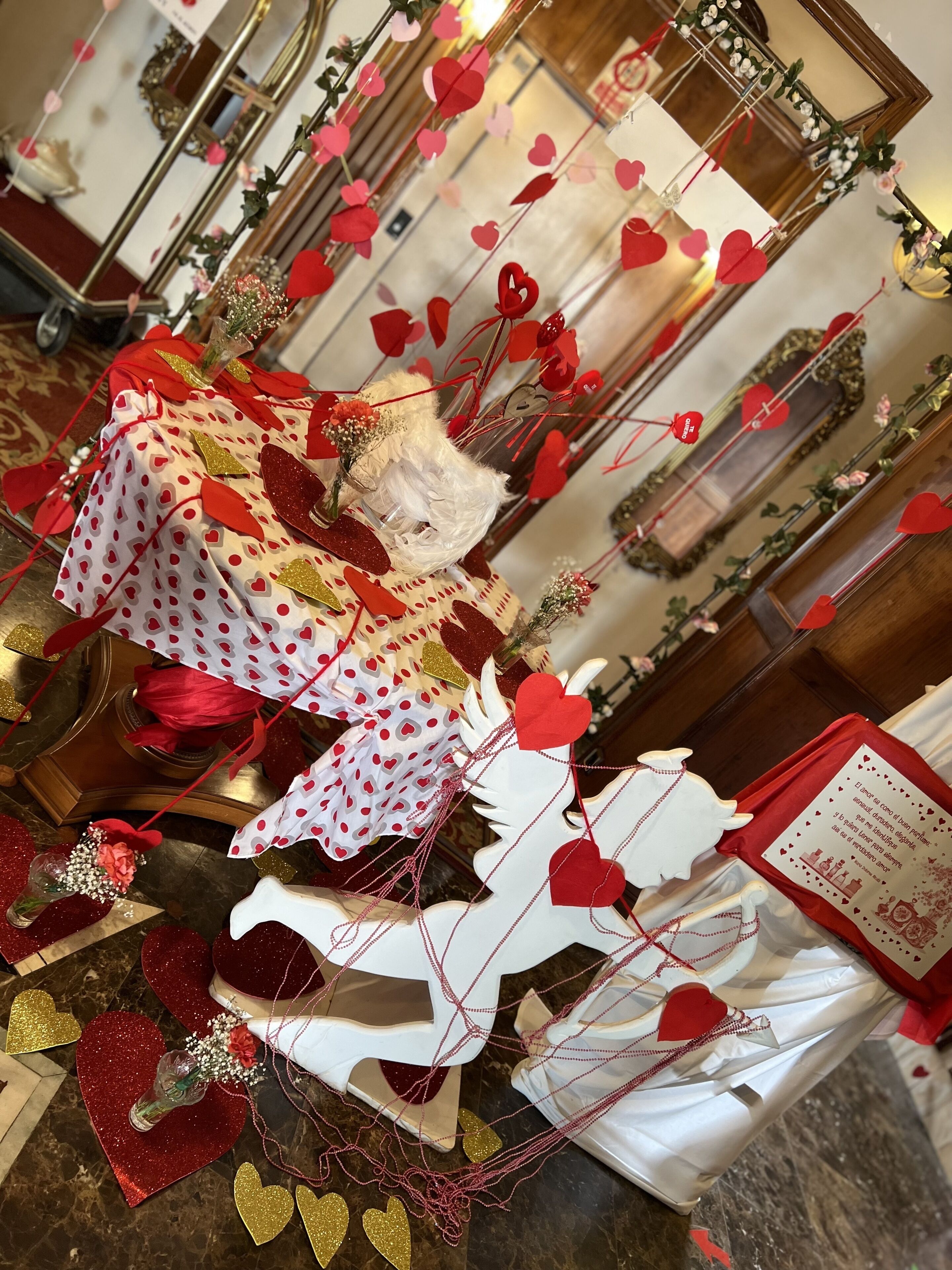 A room with a table covered in a polka dot tablecloth, surrounded by red and gold heart decorations, and a white decorative piece resembling a bird.
