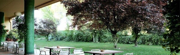 An outdoor patio area with tables and chairs, surrounded by lush greenery and trees.