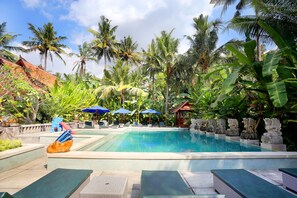 Una piscina con sillas de descanso y sombrillas, rodeada de palmeras y plantas tropicales.
