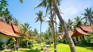 A tropical resort with palm trees, a pathway, and traditional red-roofed buildings. - Dewantara Resort Bali (Gerokgak)