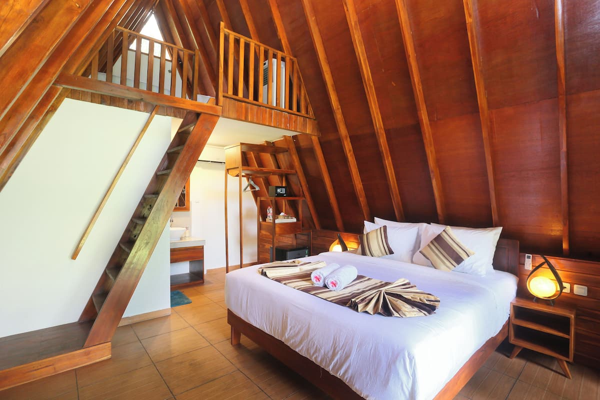 A bedroom with a wooden sloped ceiling, a bed with white bedding, a nightstand, and a small table with a lamp.