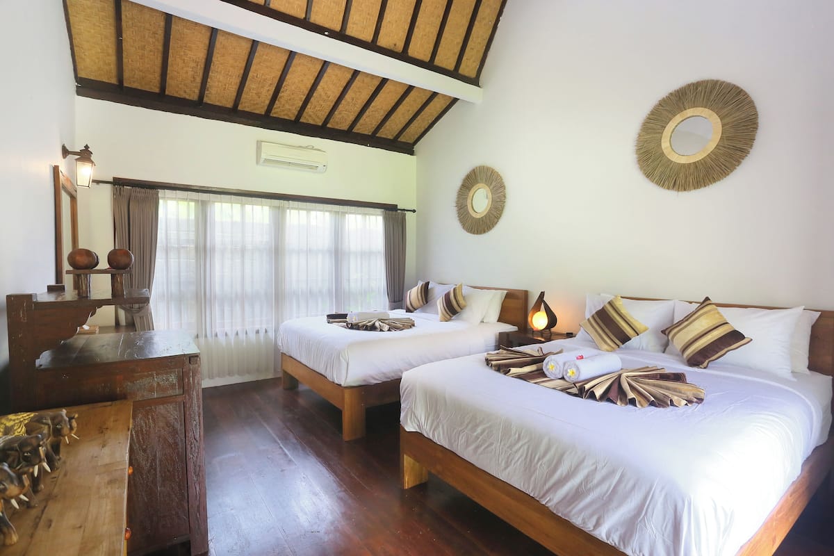 A hotel room with two beds, wooden furniture, a desk, and a large window with curtains.