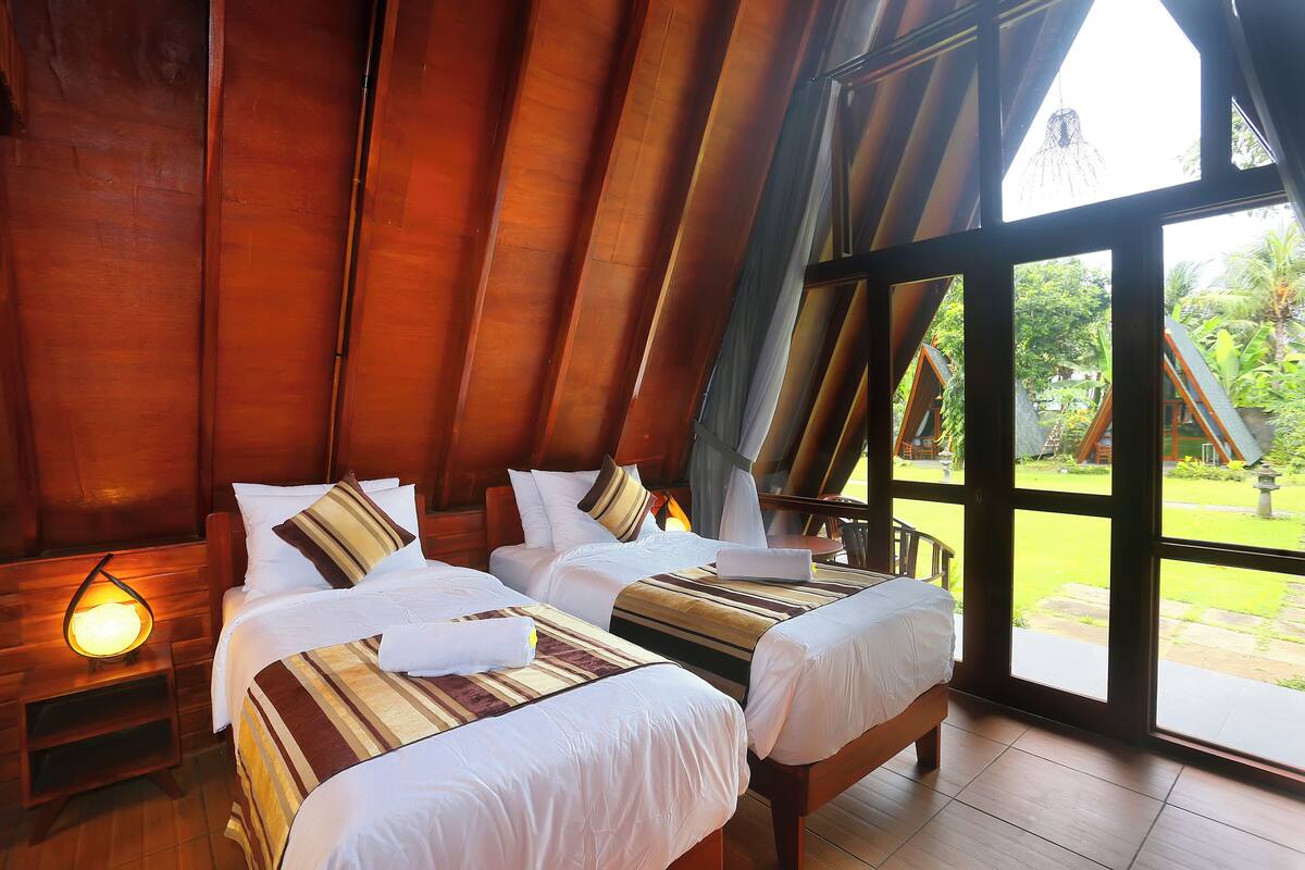 A room with two beds, wooden walls, and large windows.