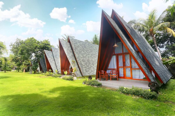 Una hilera de edificios modernos con techos triangulares, un césped cuidado y palmeras al fondo.