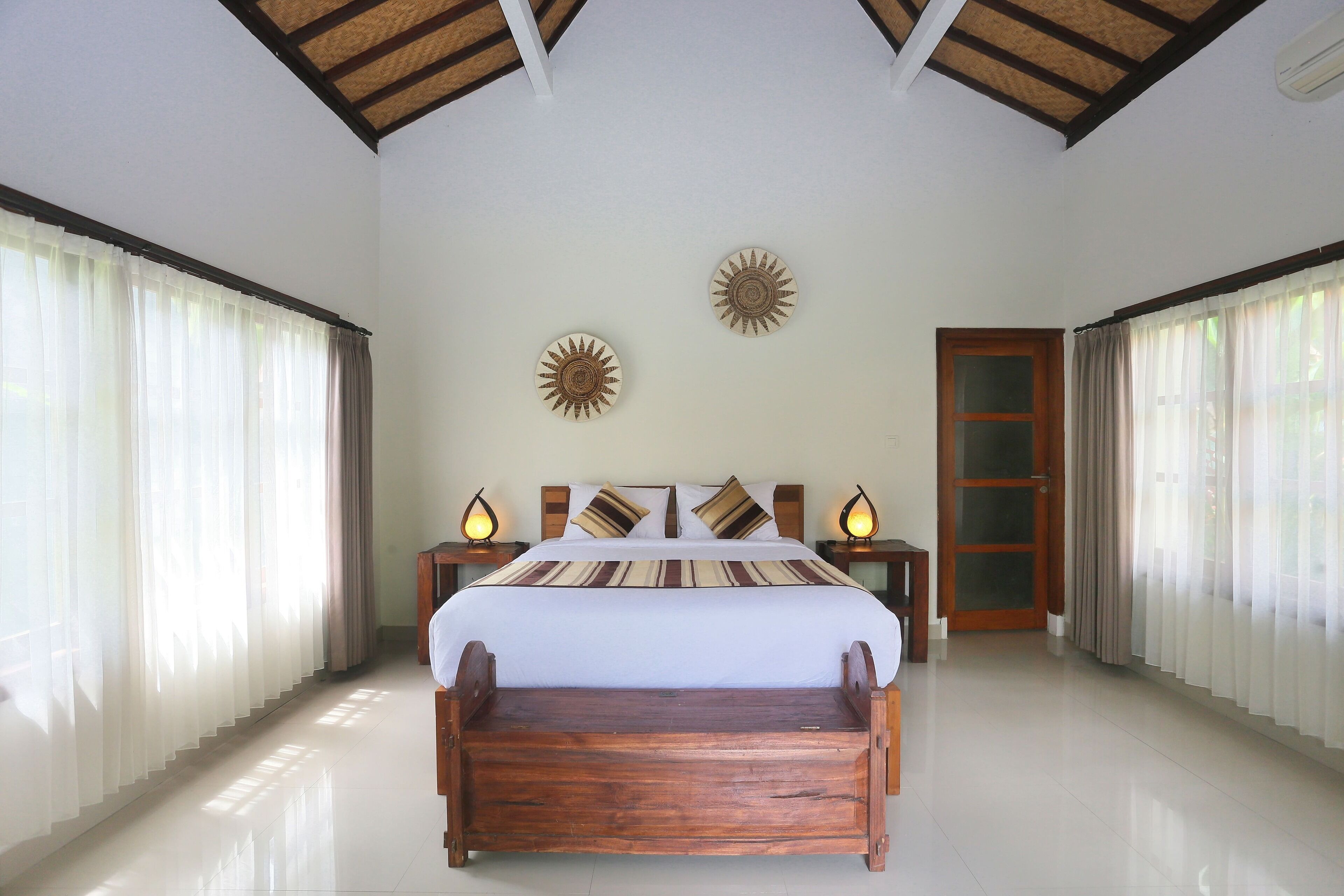 A spacious bedroom with a wooden bed, white curtains, and two wall decor pieces.