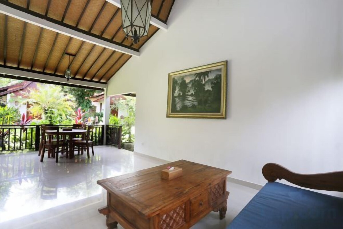 A room with a wooden table, a blue sofa, a framed picture on the wall, and a balcony with a view of greenery.