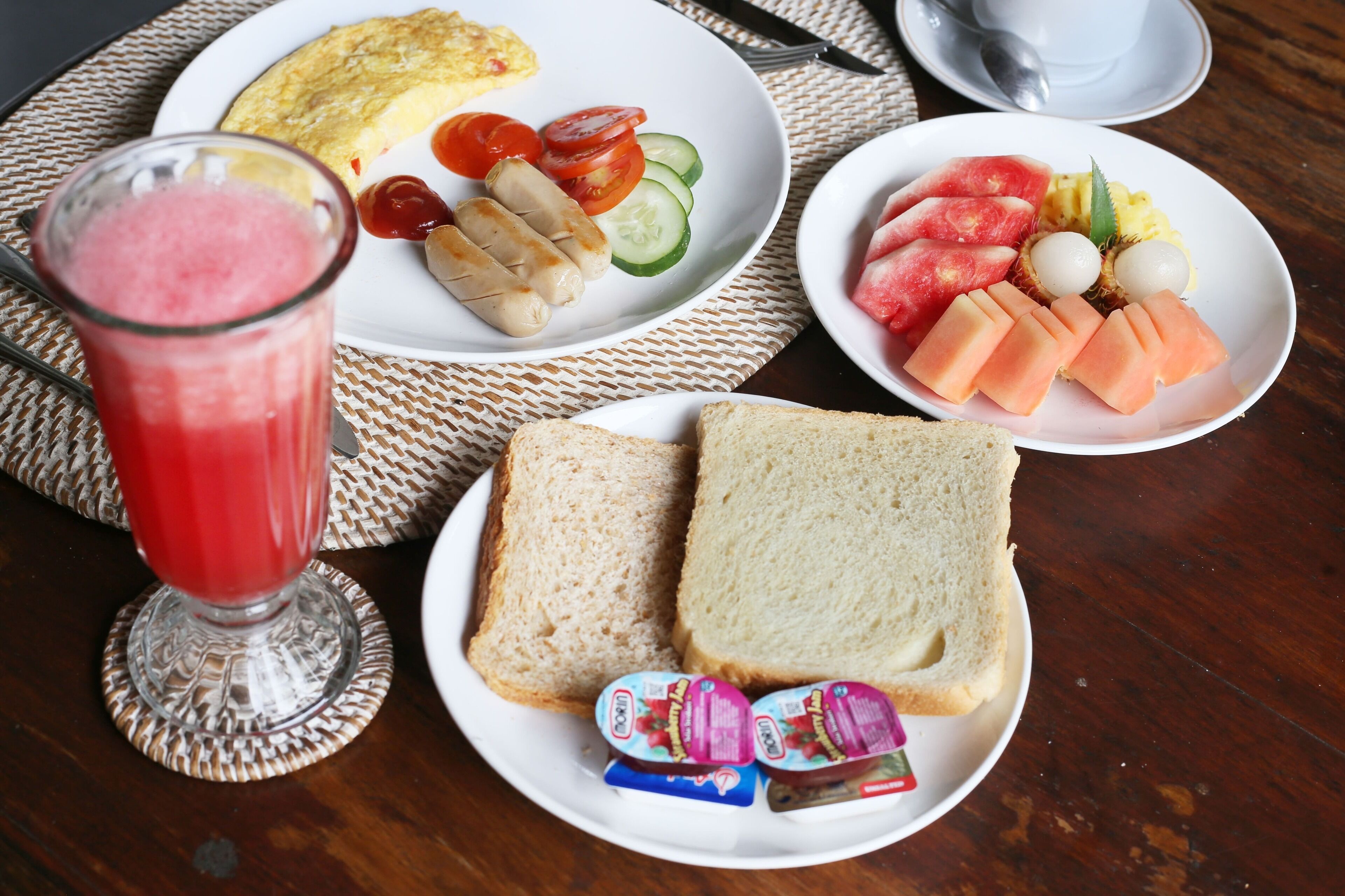 Een ontbijttafel met borden eten, waaronder toast, eieren, tomaten, komkommers en een fruitmand met watermeloen en meloen.