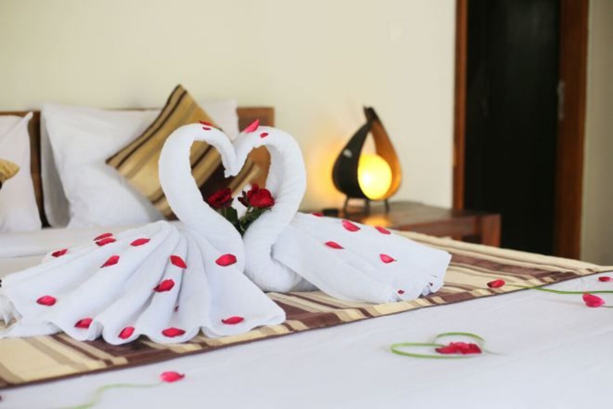 Una cama con una toalla dispuesta en forma de corazón y pétalos de rosa.