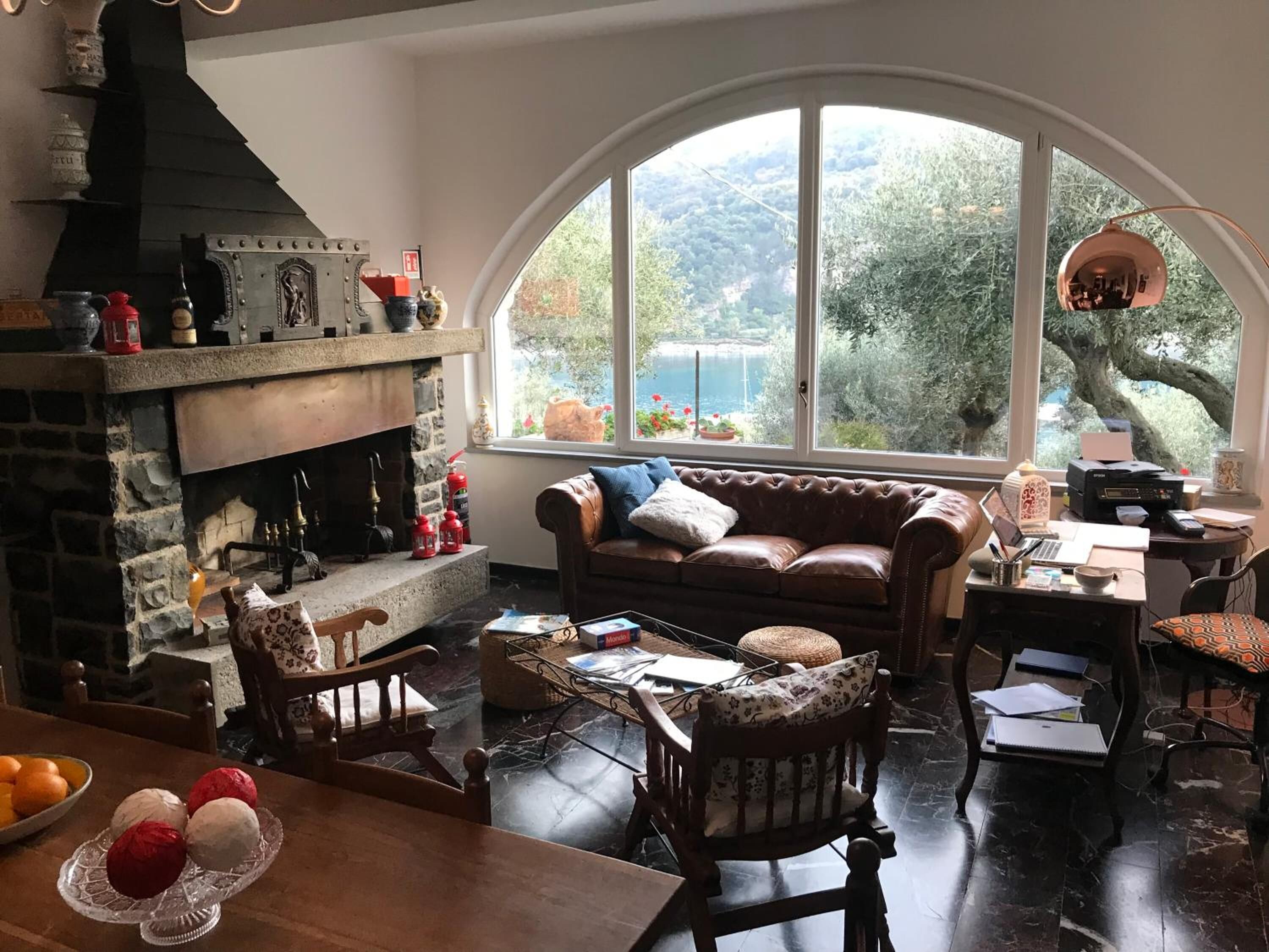 Un salon chaleureux avec une cheminée en pierre, un canapé en cuir et une grande fenêtre en arc d’où l’on peut admirer un paysage magnifique.