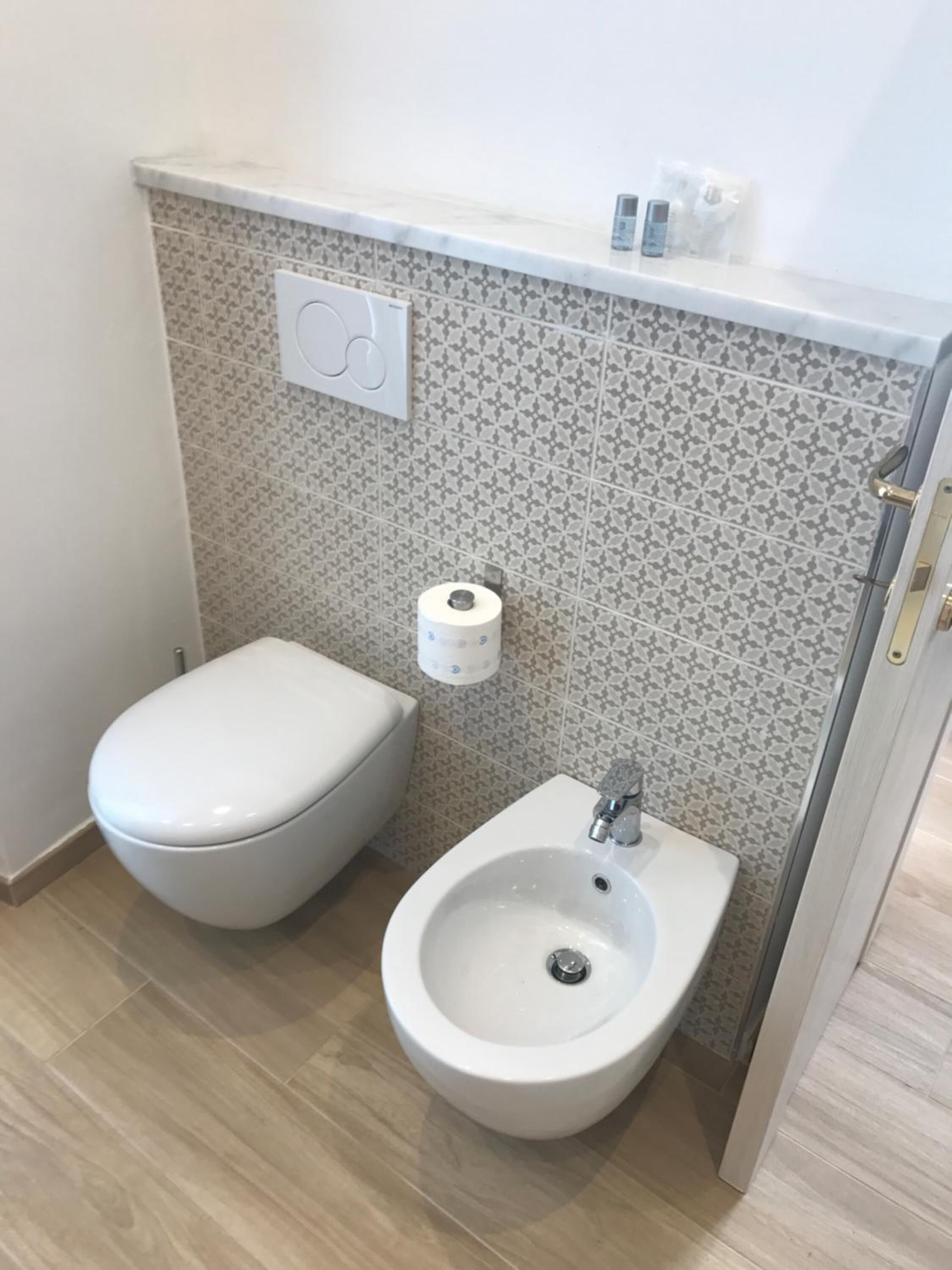 Un baño pequeño con inodoro, bidé y un dispensador de papel higiénico fijado a la pared.