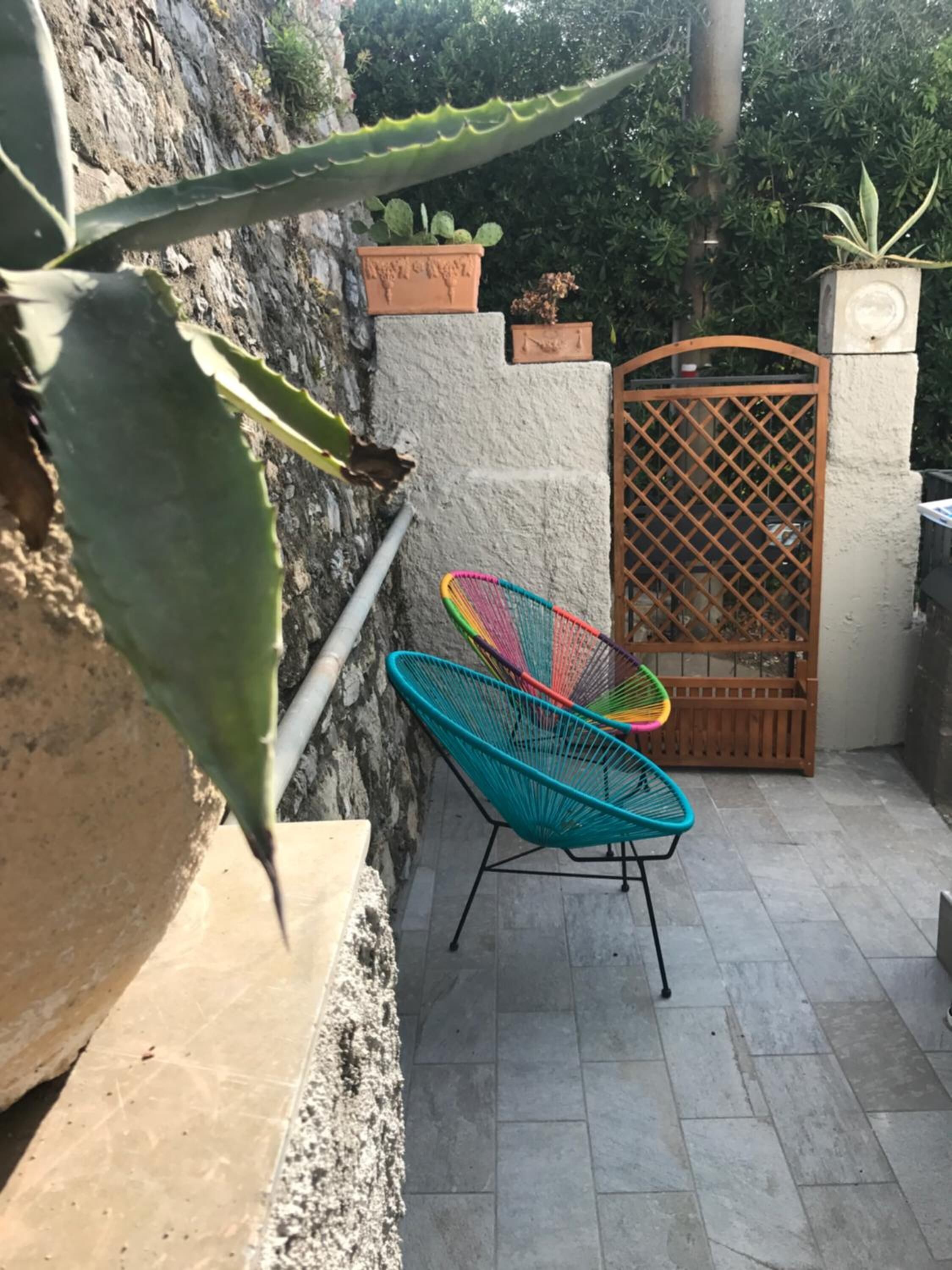 A small outdoor area with a stone wall, a metal gate, and a colorful chair.