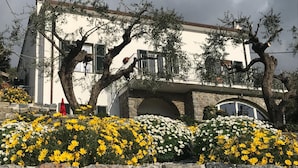A building with a stone facade, a balcony, and a garden with yellow and white flowers. - Relais Santa Caterina (Portovenere)