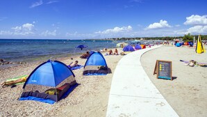 Une plage avec des tentes et des parasols, une promenade en bord de mer et un ciel dégagé.