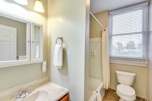 Une salle de bain équipée d’un lavabo, d’un miroir, d’un porte-serviettes, de toilettes, d’une douche et d’une fenêtre avec des stores.