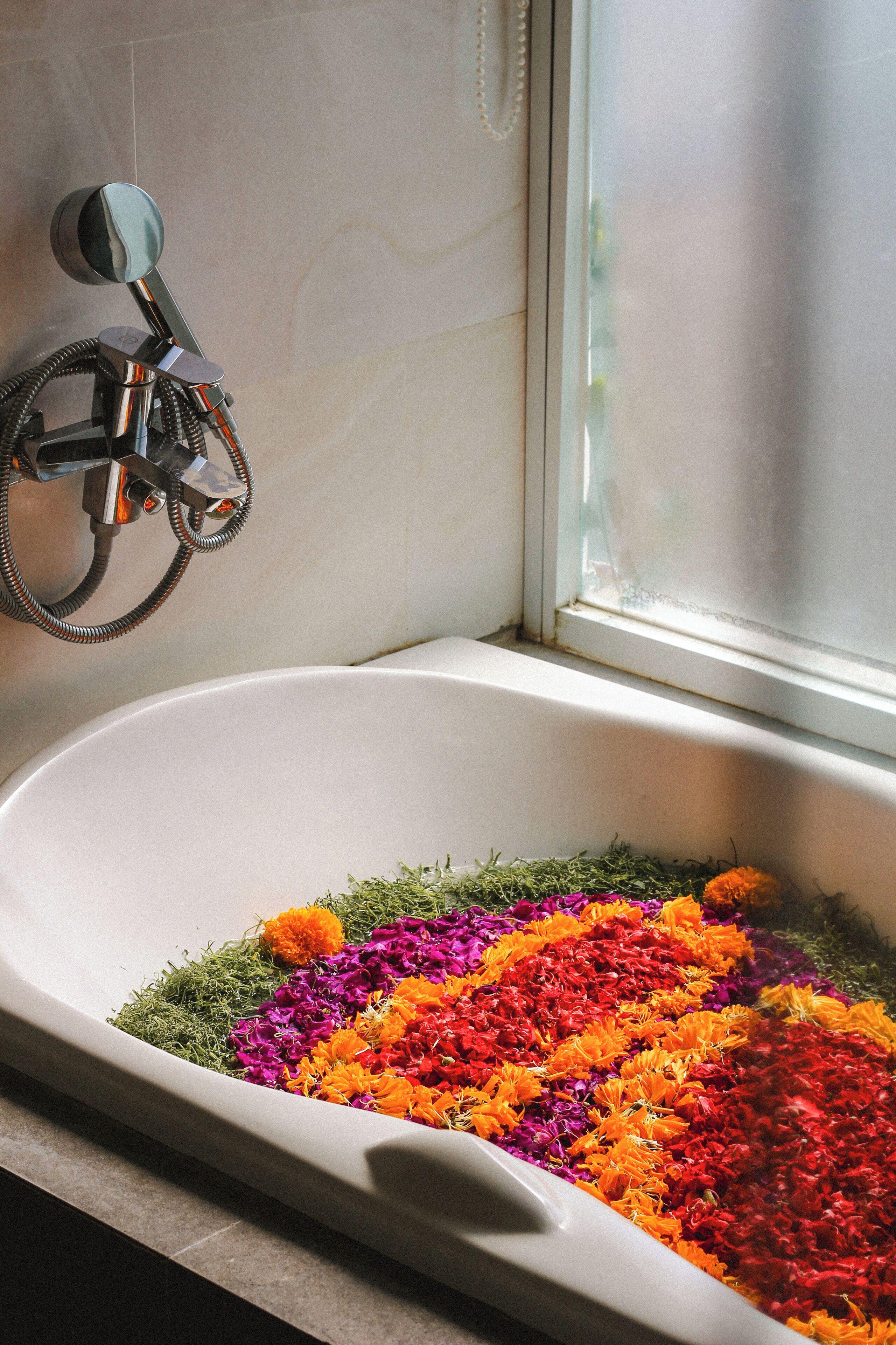 Una bañera llena de flores de colores, un cabezal de ducha y una ventana.