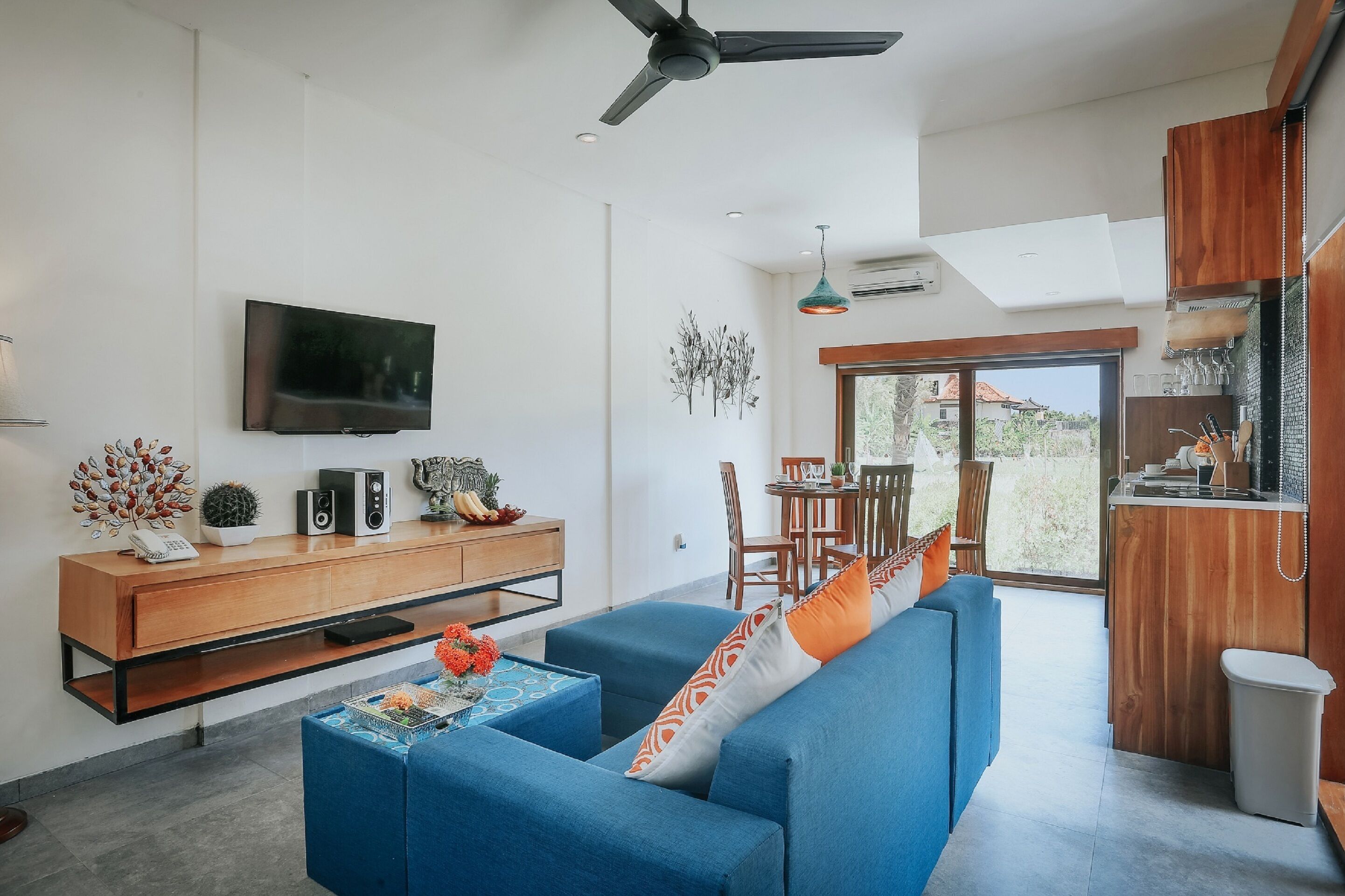 Ein modernes Wohnzimmer mit einem blauen Sofa, einem Holztische, einem Flachbildfernseher und einem Essbereich mit Tisch und Stühlen.