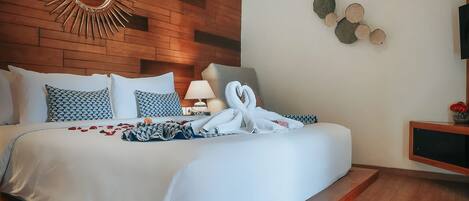 A modern bedroom with a wooden headboard, a large mirror, a bed with white linens, and a small bedside table with a lamp.