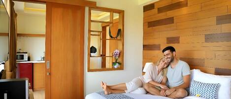 A bedroom with a wooden headboard, a bed with patterned bedding, a bedside table, and a mirror.