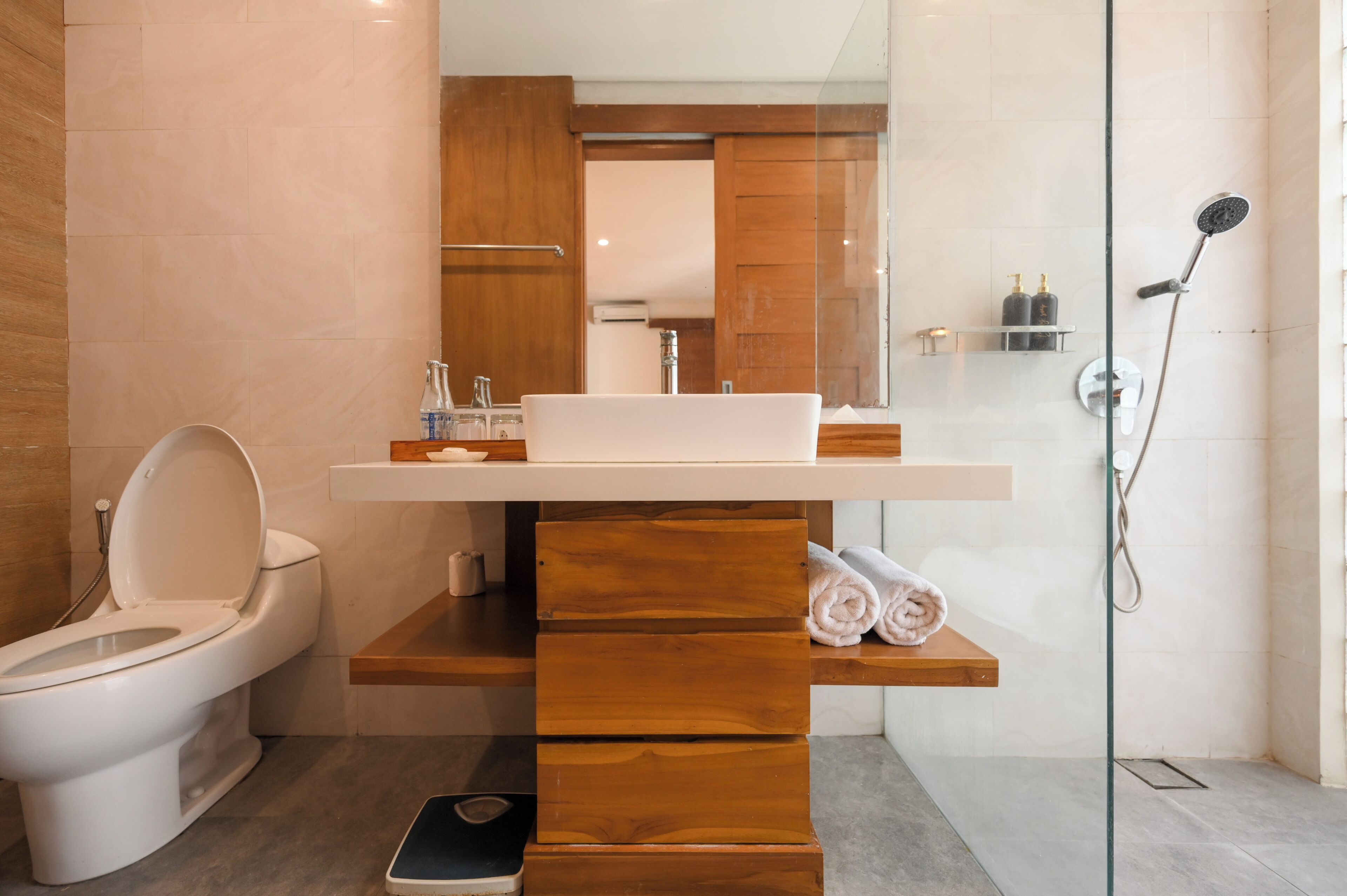 A modern bathroom with a white toilet, a wooden vanity, a sink, and a glass shower enclosure.