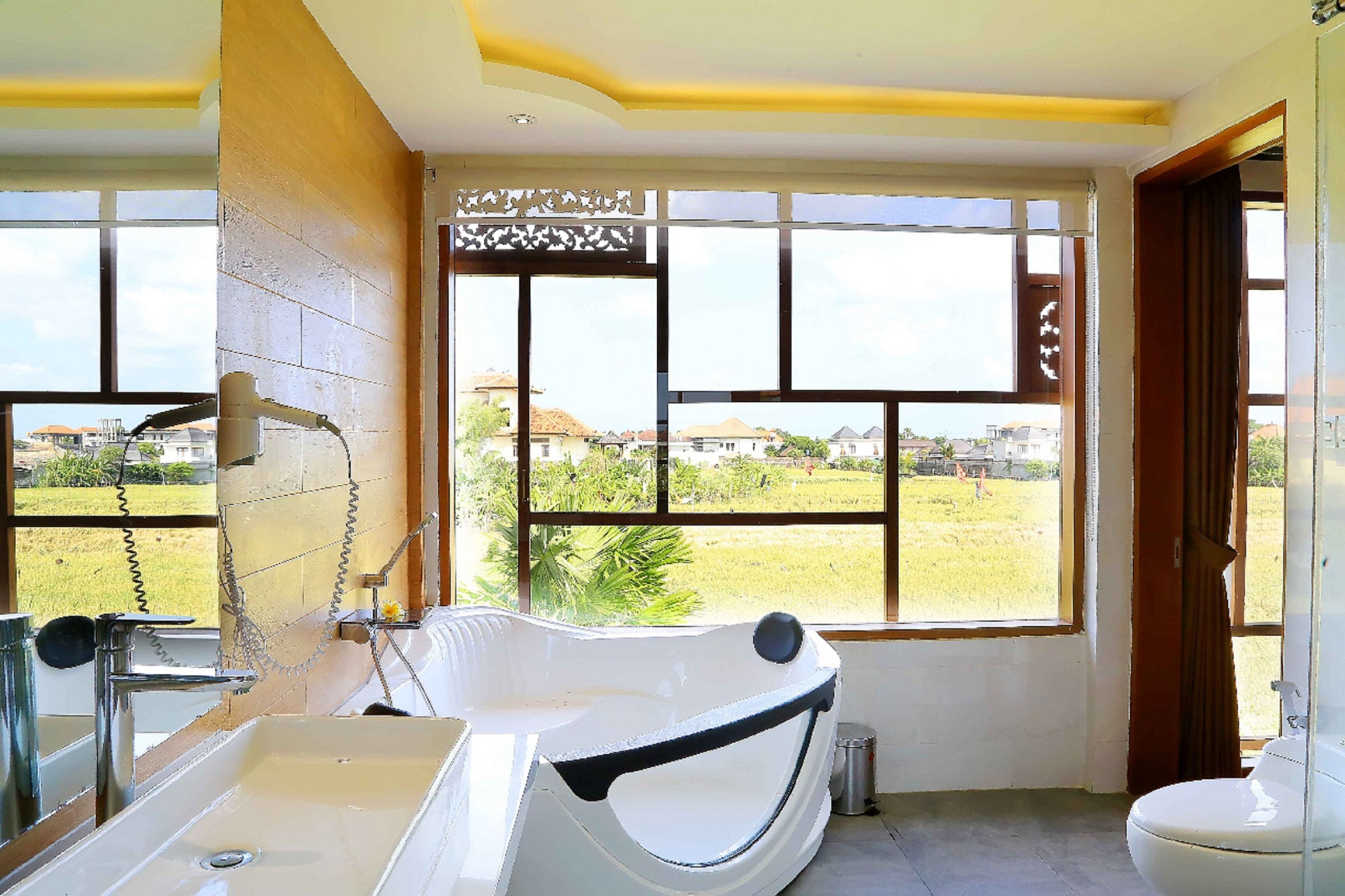 Une salle de bain avec une baignoire, un lavabo et des toilettes. Une grande fenêtre offre une vue sur un quartier résidentiel.