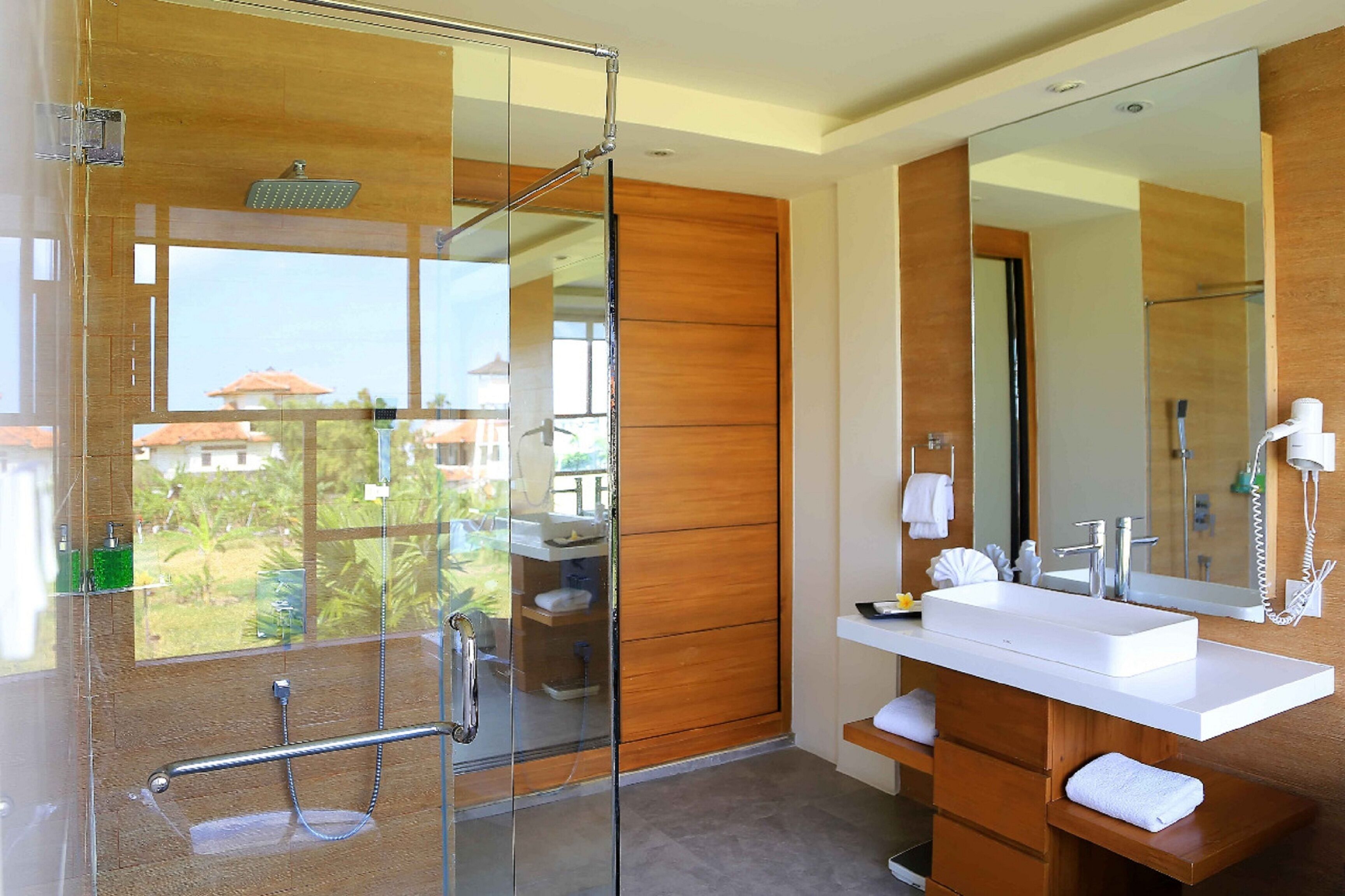 A modern bathroom with a glass-enclosed shower, a wooden vanity with a large mirror, and a view of the outdoors.