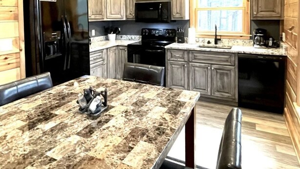 Una cocina con armarios de madera, un refrigerador negro, un microondas, una estufa y una mesa con bancos.
