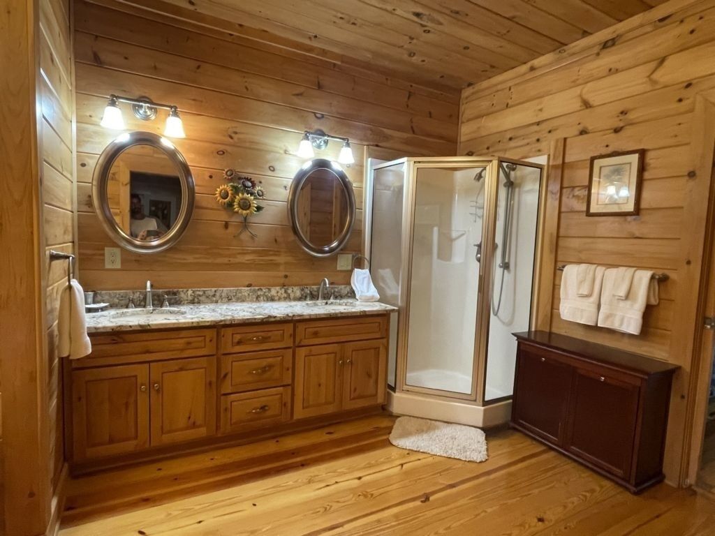 Ein Badezimmer in einer Holzhütte mit Dusche, zwei Waschbecken und einem Waschtisch.