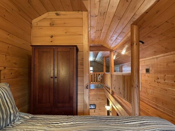 Interior de una cabaña de madera con una cama, un armario y una escalera que sube a un nivel superior.