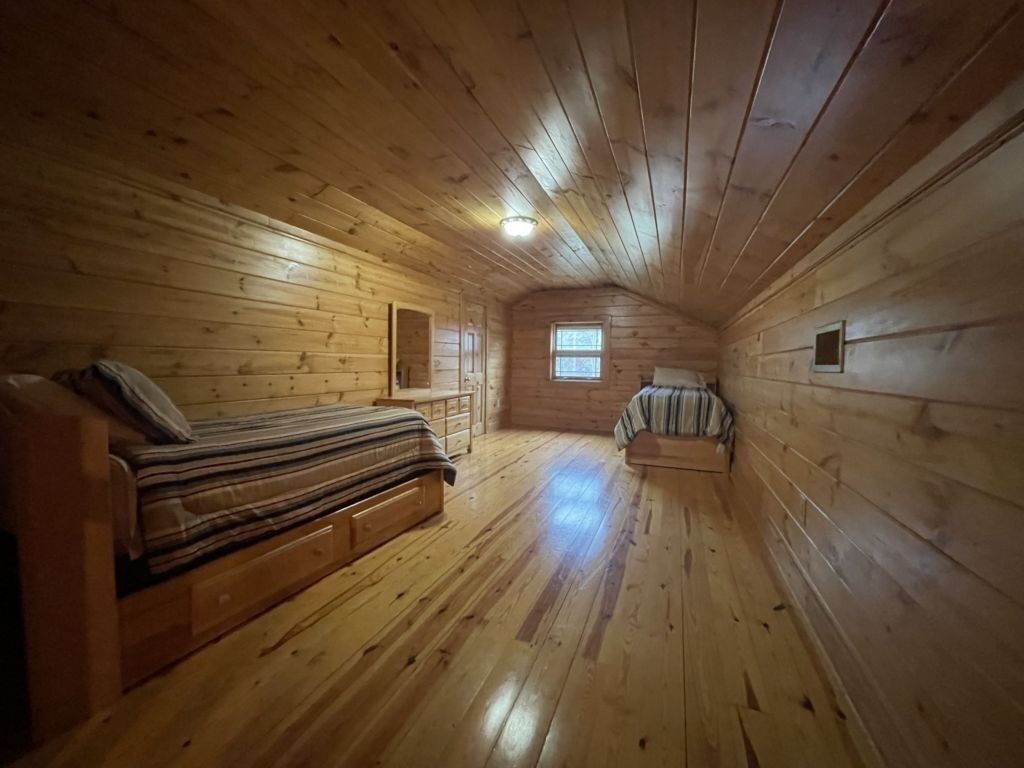 A log cabin room with a bed, a bench, and a window.
