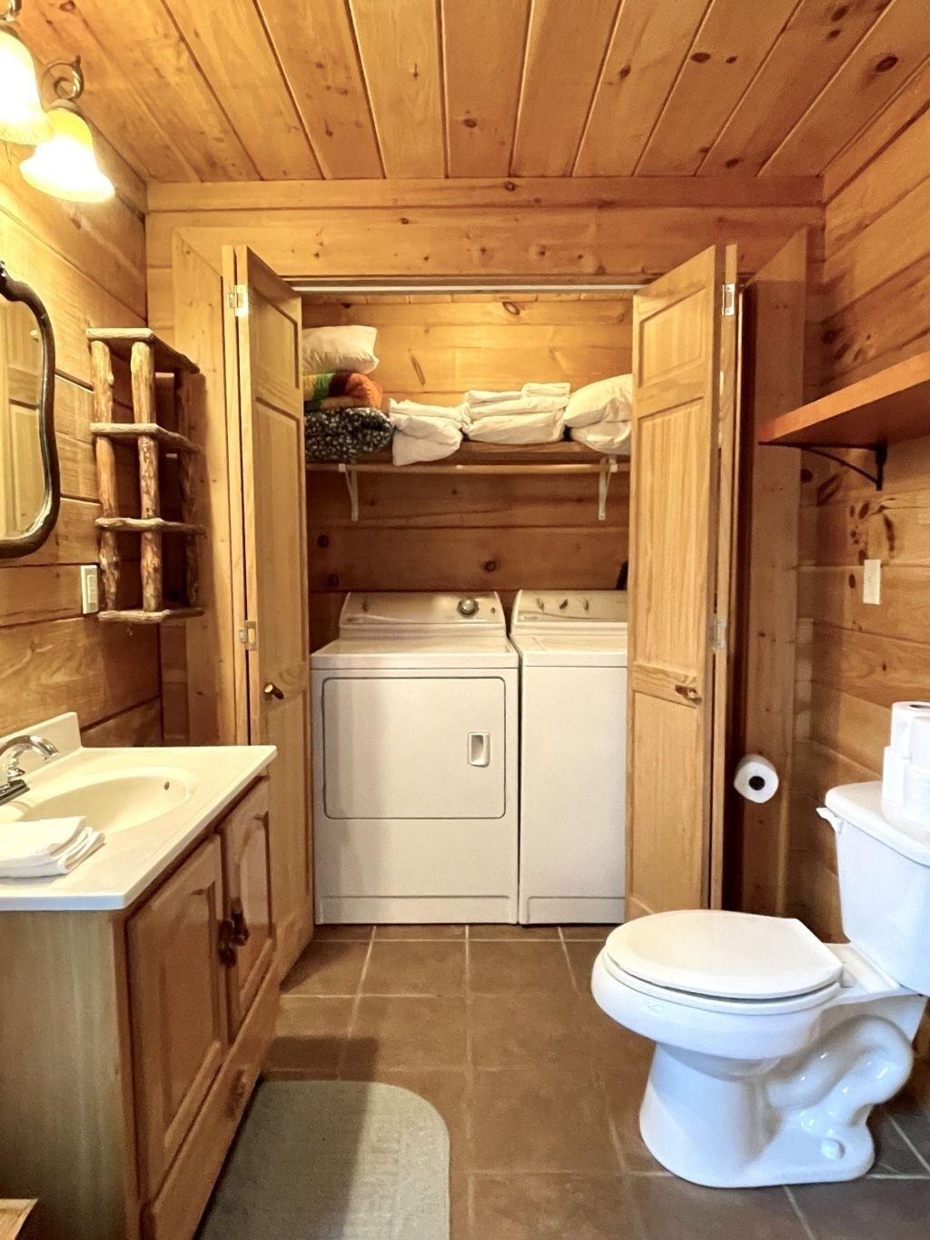 A compact wooden bathroom with a sink, toilet, and stacked washer-dryer unit.