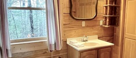 Ein Badezimmer einer Holzhütte mit Fenster, Waschbecken, Spiegel und einer Bank.