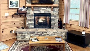 Ein gemütliches Wohnzimmer mit Kamin aus Stein, einem flachbildfernseher darüber und einer bequemen Sitzecke mit Sofa und Couchtisch.