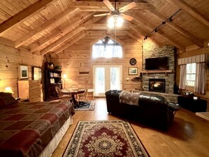 A log cabin interior with a wooden ceiling, a fireplace, a dining area, and a bedroom with a large bed. - Romantic, pet friendly cabin with private hot tub, washer/dryer and full kitchen Studio Cabin by RedAwning (Tellico Plains)