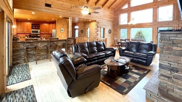 A spacious living area with leather sofas, a coffee table, and a stone fireplace. - A true log cabin with 360 degree mountain views - Pet and Motorcycle friendly! 5 Bedroom Cabin by RedAwning (Tellico Plains)
