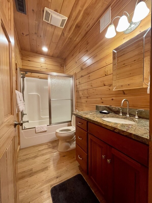 A wooden-paneled bathroom with a bathtub, toilet, and vanity with a sink and mirror.