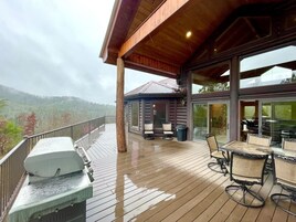 A wooden deck with outdoor furniture, a grill, and a glass-enclosed area with chairs.