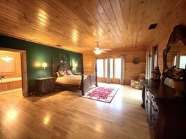 A wooden cabin bedroom with a bed, nightstands, a dresser, and a large window.