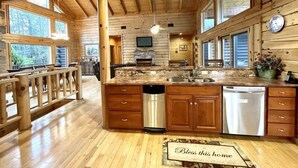 A spacious kitchen with wooden cabinets, a large island with a sink, and a built-in television. - A true log cabin with 360 degree mountain views - Pet and Motorcycle friendly! 5 Bedroom Cabin by RedAwning (Tellico Plains)