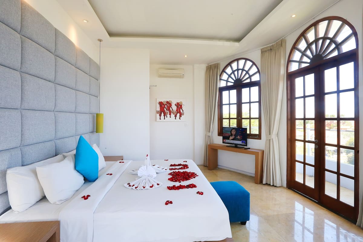 Une chambre d’hôtel avec un grand lit, une télévision et une vue sur l’extérieur grâce à de grandes fenêtres en arc de cercle.