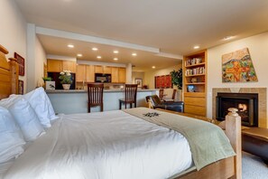 Quarto com uma cama grande, lareira, área de cozinha e estante de livros.