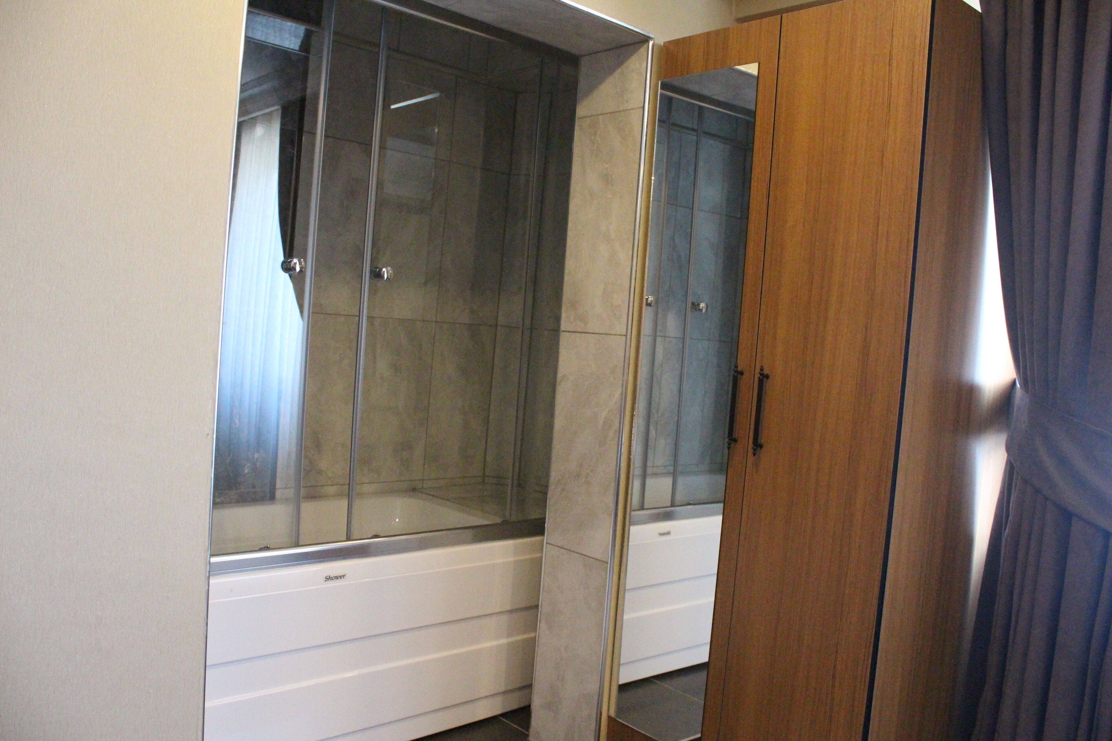 A bathroom with a glass shower enclosure, a wooden wardrobe, and a mirror.