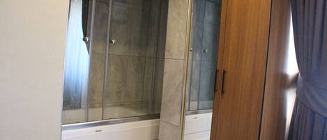 A bathroom with a glass shower enclosure, a wooden wardrobe, and a mirror.