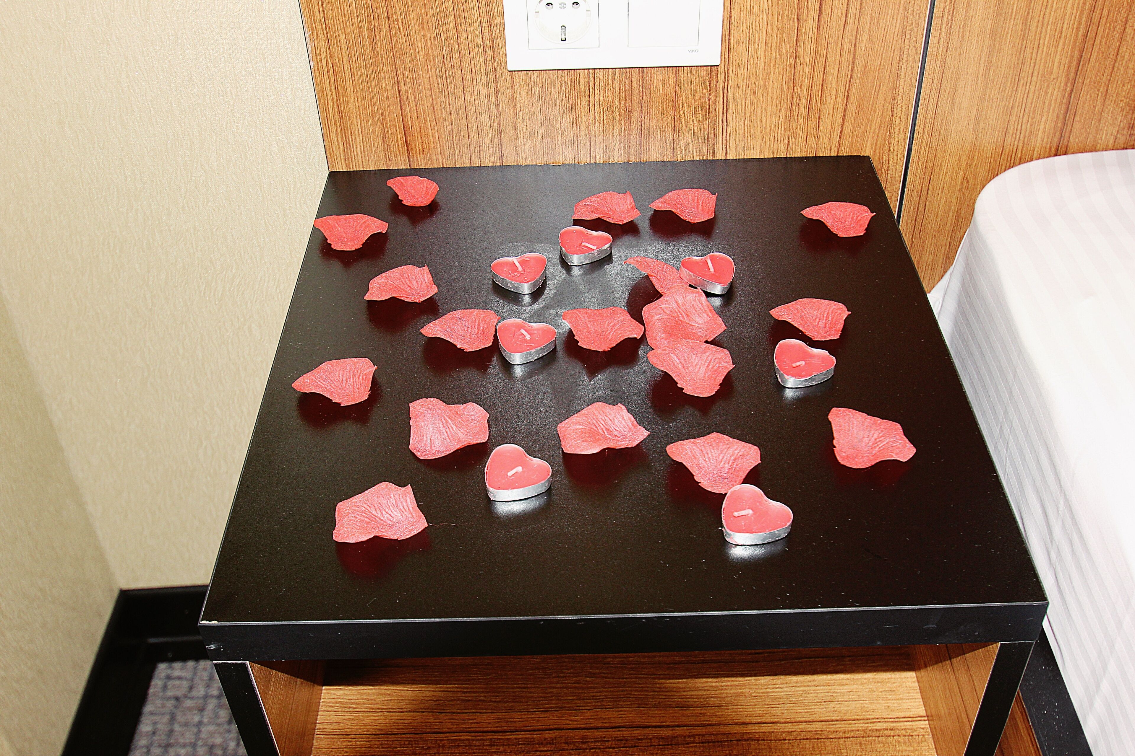A room with a bed, a wooden nightstand, and a table with heart-shaped candles.