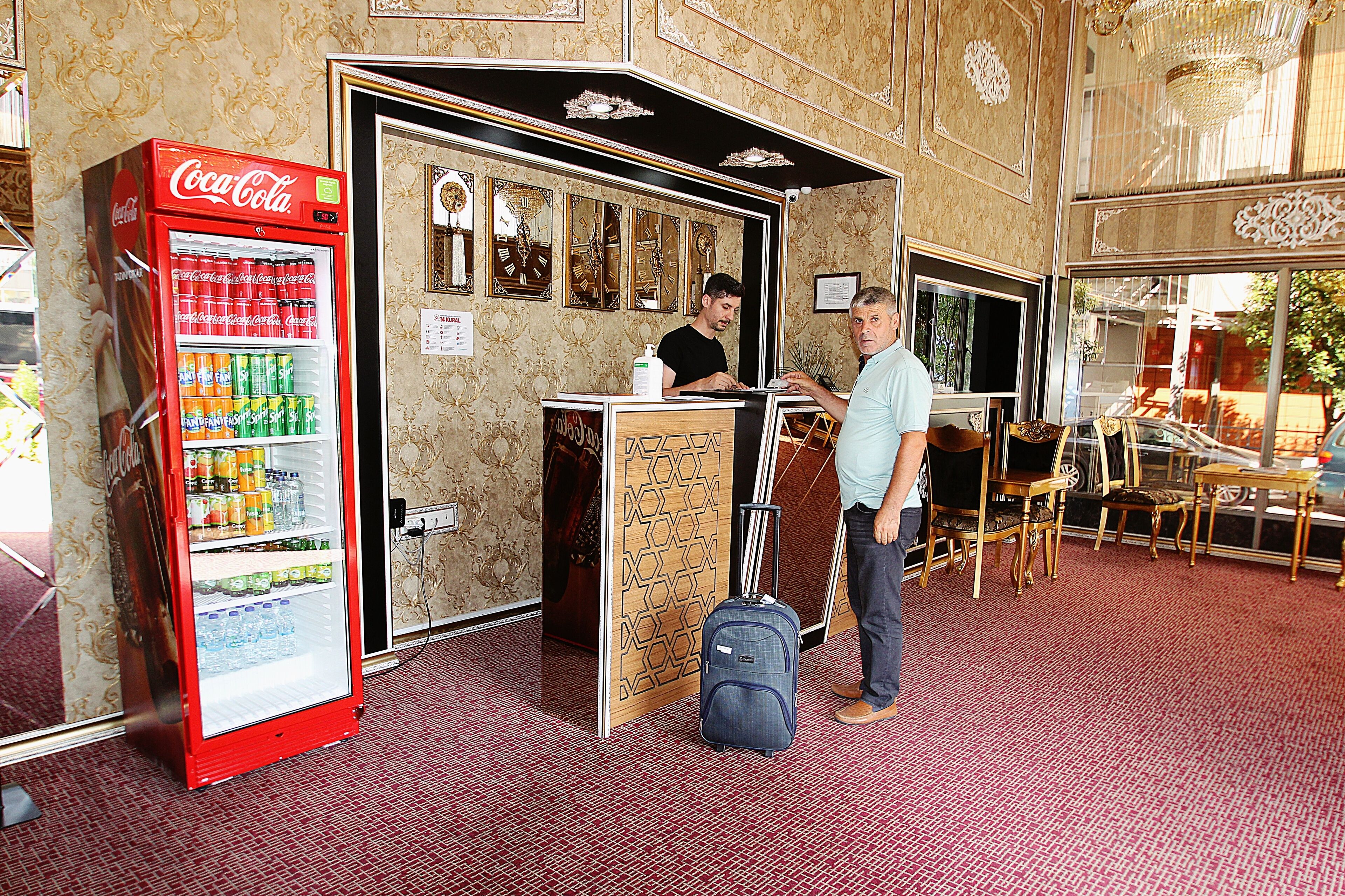 A hotel lobby with a Coca-Cola vending machine, a reception desk, and a seating area with tables and chairs.