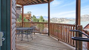 Un terrazzo in legno con tavolo e sedie, affacciato su un paesaggio montuoso.