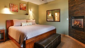 Una camera da letto con un letto grande, una panca, una ventola a soffitto, opere d'arte a parete, un caminetto e uno specchio.