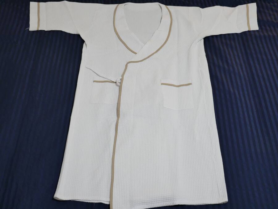 A white robe with gold trim and pockets, laid out on a dark blue bedspread.