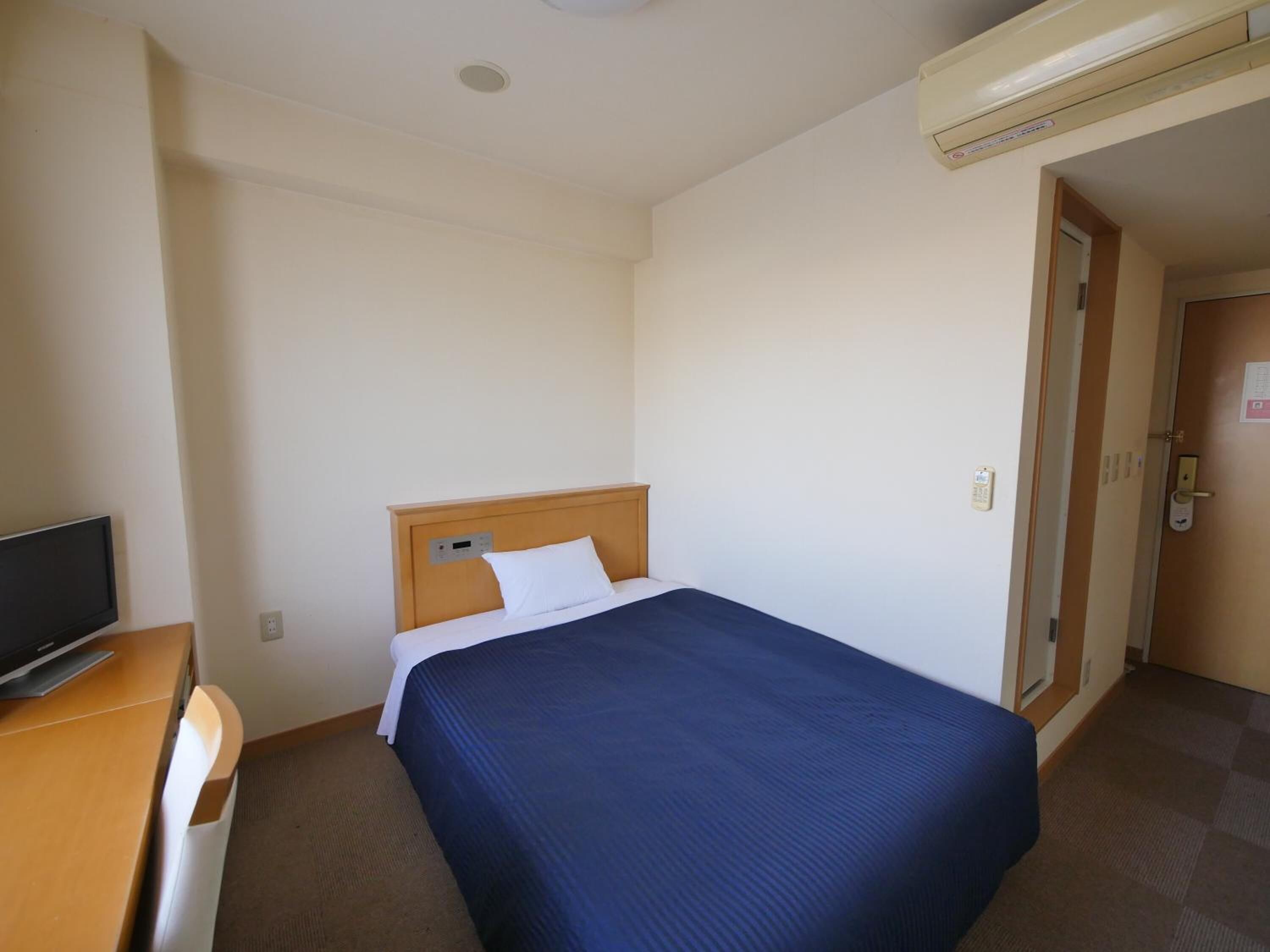 A hotel room with a single bed, a desk with a television, and a door leading to another room.