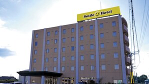 C’est un hôtel avec une enseigne jaune sur laquelle on peut lire « Smile Hotel ». Il comporte plusieurs étages et toutes les fenêtres ont la même forme.